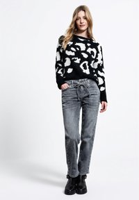 Maglione a righe bianche e nere con una vestibilità ampia, abbinato a jeans grigi con vita regolabile da coulisse, e stivaletti neri fino alla caviglia.