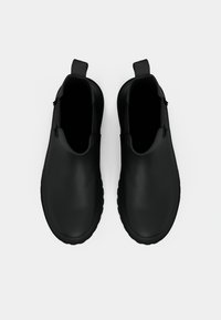 Botas de tornozelo em borracha preta com textura lisa, com puxadores no calcanhar e bico arredondado. Apresentam uma sola texturizada e flexível para melhor aderência.