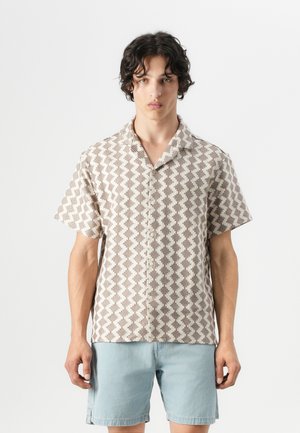 Chemise à manches courtes en beige clair avec un motif géométrique marron, dotée d'un col en V et de boutons sur le devant. Design décontracté avec une coupe ample.