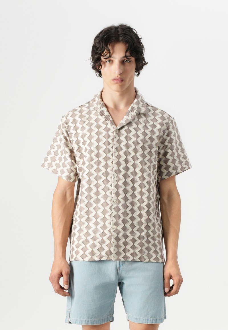 Short-sleeve shirt in light beige with a geometric brown pattern, featuring a notched collar and front buttons. Casual design with open fitting.