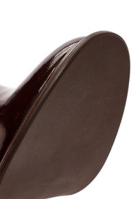Talons de chaussures en cuir verni bourgogne avec un design incurvé. La semelle est en caoutchouc marron texturé, offrant adhérence et durabilité.