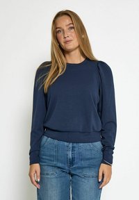 Námořnický modrý dlouhý rukáv top s kulatým výstřihem, který má zdobené ramena a přiléhavý pas, vyrobený z měkkého, elastického materiálu.