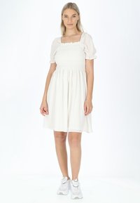 Witte korte jurk met een gerimpelde buste en pofmouwen, met een vloeiende rok. Gepaard met witte sneakers. Glad, lichtgewicht materiaal.