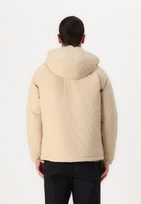 Beige puffjakke med hætte og elastiske manchetter. Glat tekstur, let krøllet stof og cropped design.