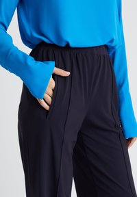 Marineblauwe slim-fit broek met elastische tailleband en zijzakken, gecombineerd met een felblauwe blouse met lange mouwen van gladde stof.