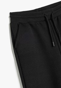Zwarte textuur joggingbroek met een geribbelde tailleband, een trekkoord en zijzakken. De stof heeft een subtiel patroon.