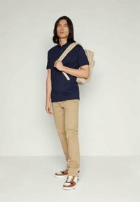 Camisa de polo azul marino, pantalones beige, zapatillas multicolores y una mochila beige. Ajuste casual con un diseño sencillo y acentos en las zapatillas de colores contrastantes.