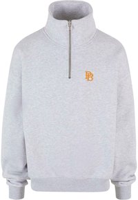 Lys grå zip-neck hettegenser med ribbestrikket mansjetter og kant. Har brodert oransje "PB"-logo på brystet. Myk stofftekstur.