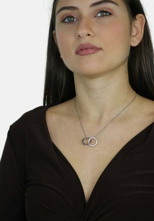 Collana in argento con due anelli intrecciati: uno liscio e metallico, l'altro decorato con pietre trasparenti.