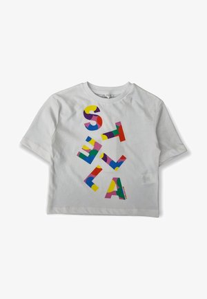 T-shirt blanc à manches courtes avec de grandes lettres multicolores formant « STELLA » disposées verticalement sur le devant.