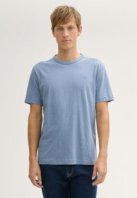 Tricou albastru deschis din bumbac moale, cu guler rotund, mâneci scurte și un detaliu grafic mic pe piept.