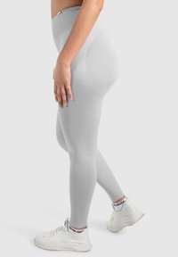 Leggings gris clair avec une taille haute et une texture côtelée, associés à des chaussures de sport blanches avec des accents de marque contrastés.