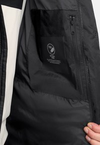 Zwarte donsjacket interieur met een gladde textuur. Beschikt over een ritszak en een label dat 700 fill power natuurlijke donsisolatie aangeeft.