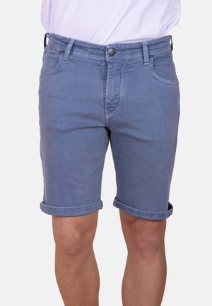 Pantalones cortos azules con dobladillo enrollado, usados por una persona con piernas visibles y una camisa blanca metida por dentro.