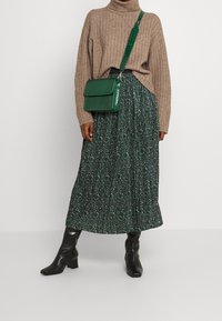 Zelená plisovaná sukně se zlatými jiskřičkami, béžový žebrovaný svetr, černé kozačky na podpatku a zelená kabelka přes rameno s krokodýlím vzorem.