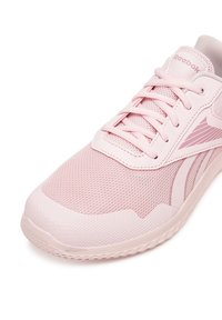 Pantofii sport roz deschis au un superior din plasă, șireturi plate și o talpă din cauciuc texturată, cu un logo Reebok pe lateral.