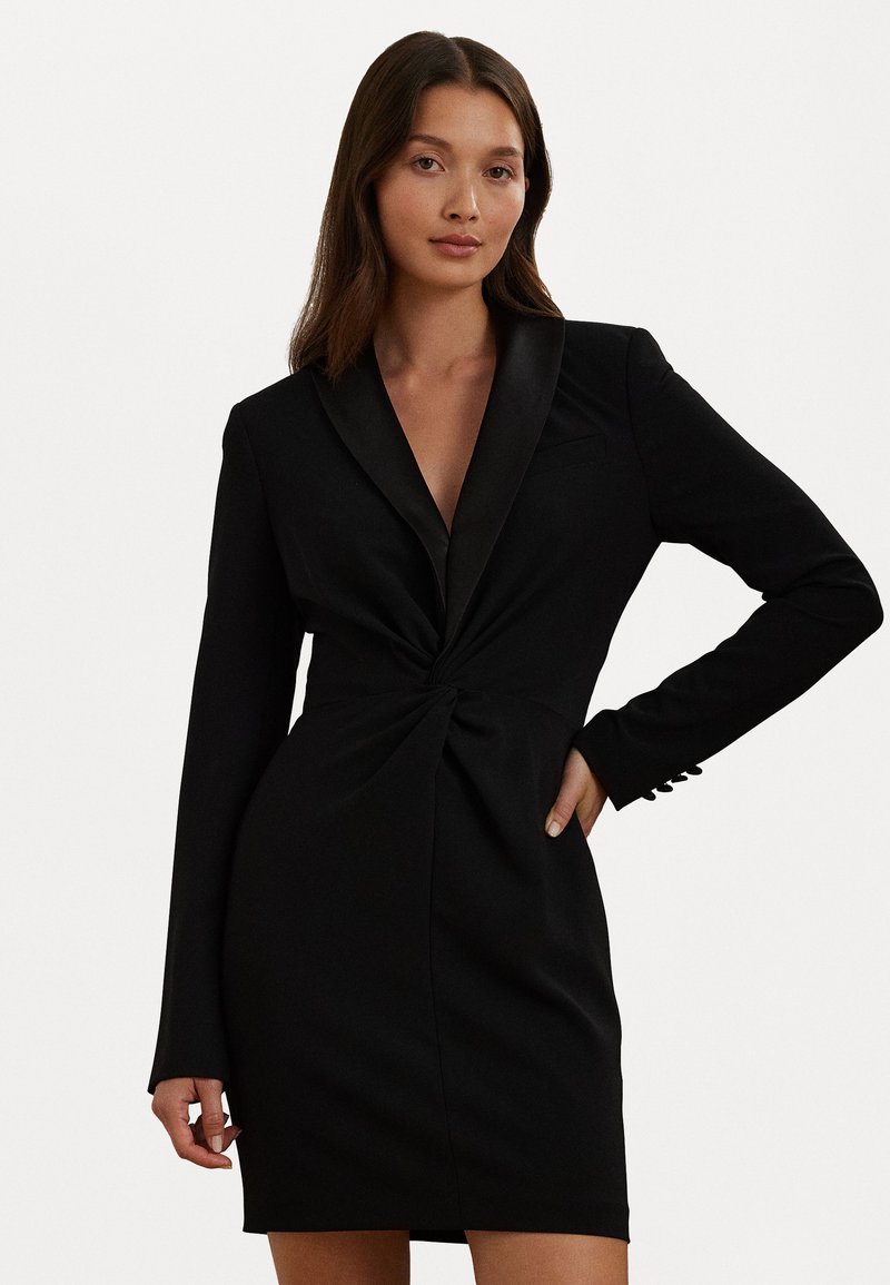 Vesti preto com um decote em V profundo e mangas longas. Apresenta um design torcido na cintura e detalhes em cetim na gola.