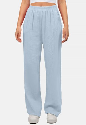 Pantaloni ampi blu chiaro in tessuto testurizzato con cintura elastica e tasche laterali, abbinati a sneakers bianche.