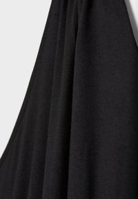 Gros plan d'un tissu noir lisse suspendu avec des coutures visibles le long du bord sur un fond clair.