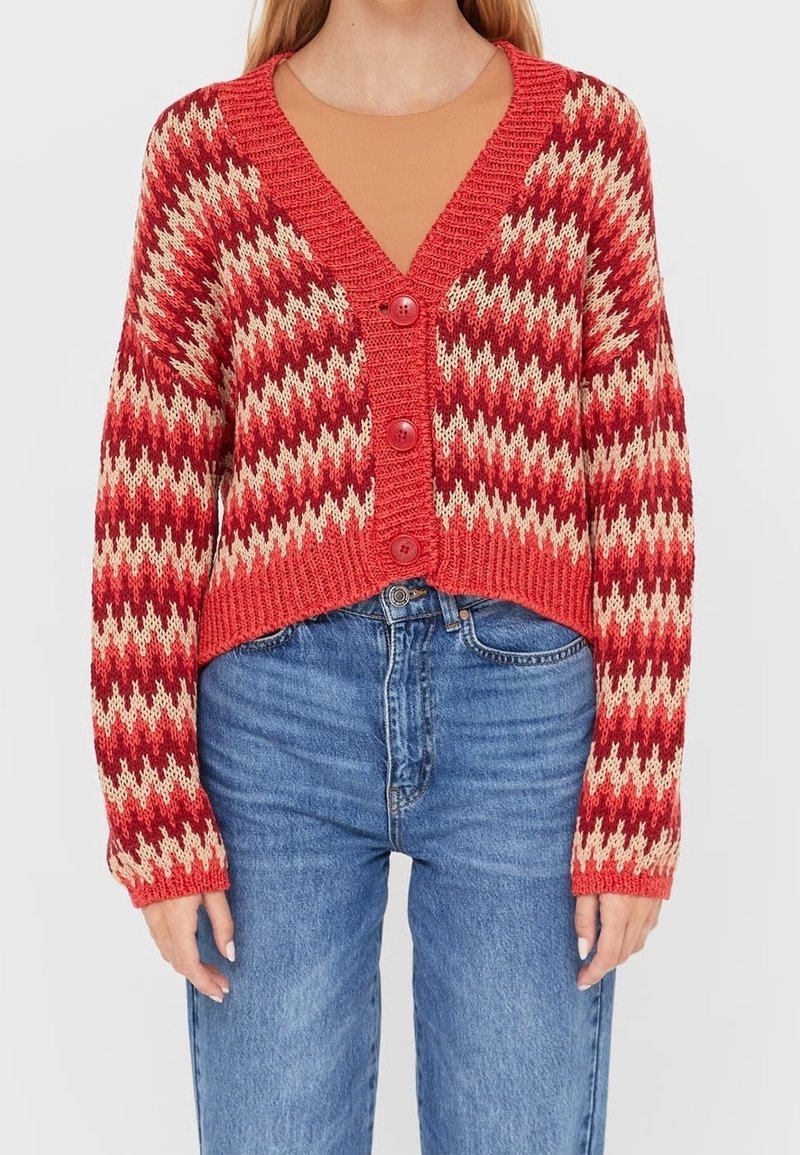 Cardigan en tricot à motif zigzag rouge et crème avec un décolleté en V, une coupe courte et trois boutons à l'avant. Jean en denim bleu classique.