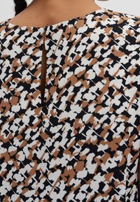 Mønstret kjole med et brun, hvid og sort abstrakt print og en nøglehulåbning i ryggen. Lavet af tekstureret stof.