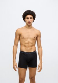Sorte bomuldsboxershorts med elastisk linning med mærket "TOMMY HILFIGER" logo i hvidt og rødt.