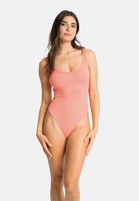 Maillot de bain une pièce côtelé corail avec un décolleté arrondi, des bretelles fines, des cuisses haute et une texture lisse. Aucun accent ni motif notable.