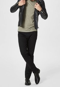 Svart läderjacka över en grön skjorta, svarta slim-fit byxor och svarta ankelboots. En enkel design med släta texturer och figurnära passform.