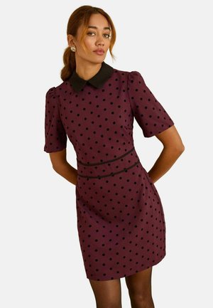Kurzarmkleid aus dunkelburgunderfarbendem Stoff mit schwarzen Punkten, einem schwarzen Kragen, strukturierten, erhobenen Ärmeln und einer definierten Taille.