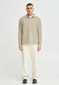 Beige poloshirt met lange mouwen en een kraag, met een comfortabele pasvorm. Gecombineerd met off-white cargobroeken en zwarte schoenen. Eenvoudig ontwerp.