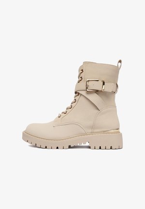 Beżowe skórzane botki za kostkę na sznurówki z grubą gumową podeszwą, złotym paskiem z klamrą i pętelką na tyle.