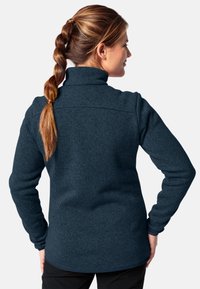 Dunkelblaues Fleece-Jacket mit hohem Kragen und langen Ärmeln, das eine strukturierte Oberfläche und eine taillierte Silhouette im Rückenbereich aufweist.