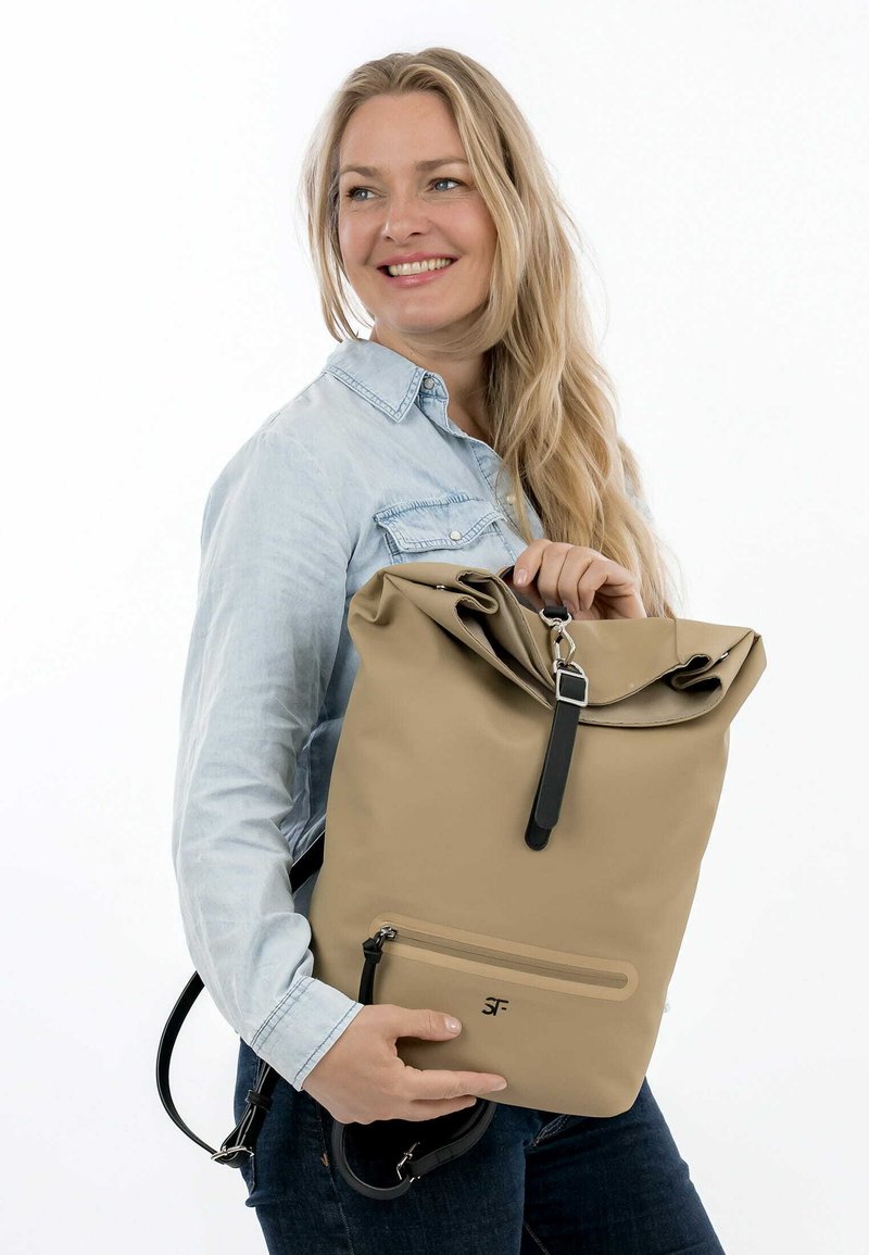 Helles beige Rolltop-Rucksack mit schwarzen Akzenten, aus strapazierfähigem Material, mit einer frontalen Reißverschlusstasche und verstellbaren Schulterriemen.