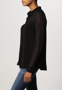 Black sheer button-up shirt with a collar, long sleeves, and a relaxed fit, paired with blue jeans. Soft fabric with a smooth texture.