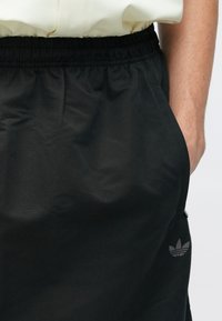 Sorte shorts med elastisk midjebånd og sidelommer, med en subtil grå logo på nedre ben. Glatt, lett stoff.