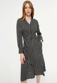 Zwart en beige patroonjurk met een v-hals, lange mouwen, tailleband en een knielange zoom met een vloeiende uitstraling.