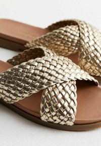 Kullanımı kolay ve rahat bir düz tabana sahip, kıvrımlı kayışlarla süslenmiş altın dokuma kaydırma terlikler, pürüzsüz kahverengi ayak tabanı ile.