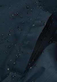 Waterdicht donker stof met een golfachtige textuur, met zichtbare waterdruppels en een horizontale naaddetail.