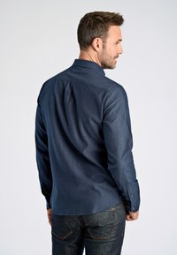 Camicia a maniche lunghe blu navy con colletto classico, piega sulla schiena e una texture liscia, abbinata a jeans in denim scuro.