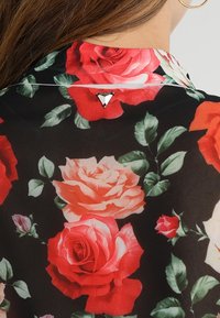 Blusa floreale con sfondo nero, caratterizzata da rose rosse e rosa, foglie verdi e un accento triangolare argento al collo.