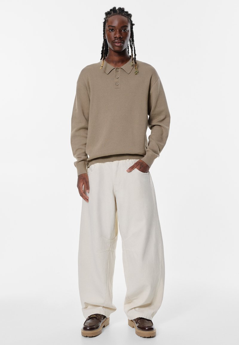 Beige pletený svetr s límcem a třemi knoflíky, doplněný volnými kalhotami v odstínu slonoviny a hnědými platformovými botami.