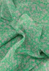Tela verde con un patrón floral en rosa pálido. La textura parece ligera y ligeramente transparente, con pliegues y curvas fluidas.
