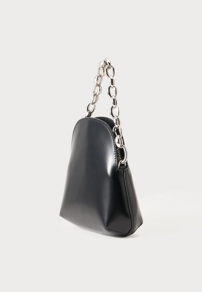 Sac à main en cuir noir avec un haut arrondi et une poignée chaîne argentée épaisse sur un fond clair uni.