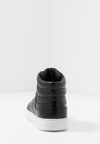 Baskets montantes en cuir noir avec un col rembourré, semelle en caoutchouc blanc et détails latéraux texturés. Fini lisse avec des accents de couture subtils.