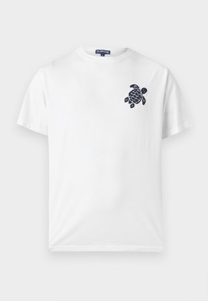 T-shirt blanc à manches courtes avec col rond, petit motif noir de tortue sur le côté gauche de la poitrine et étiquette de la marque Vilebrequin à l'intérieur du col.