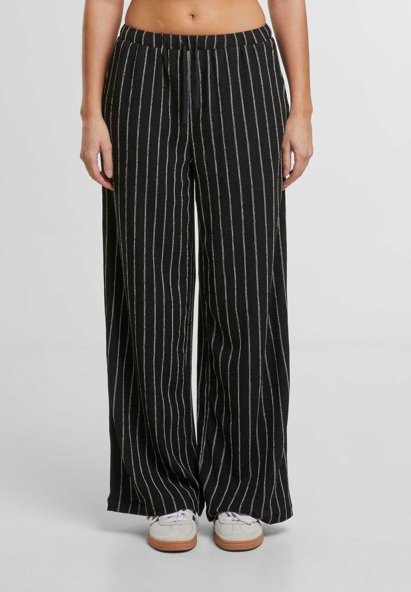 Pantaloni a gamba larga a righe bianche e nere con vita elastica e dettaglio con lacci, realizzati in tessuto texturizzato. Presentano una vestibilità ampia e fluida.