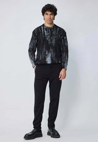 Pull noir avec un motif de rayures abstraites grises, col rond, poignets côtelés; associé à un pantalon noir et des chaussures noires.