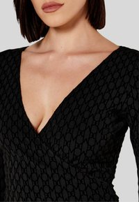 Abito avvolgente nero con scollatura a V profonda, tessuto testurizzato con un motivo sottile e maniche lunghe. Dettaglio di cucitura visibile lungo i bordi.