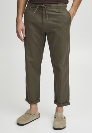 Olivgröna byxor i linneblandning med dragsko i midjan, uppvikta vid anklarna, i kombination med beigea mocka slip-on skor.