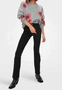 Grauer Strickpullover mit roten Blumenmustern, kombiniert mit schwarzen, engen Hosen und Stiefeletten. Weicher Stoff, lässige Passform und entspannter Stil.